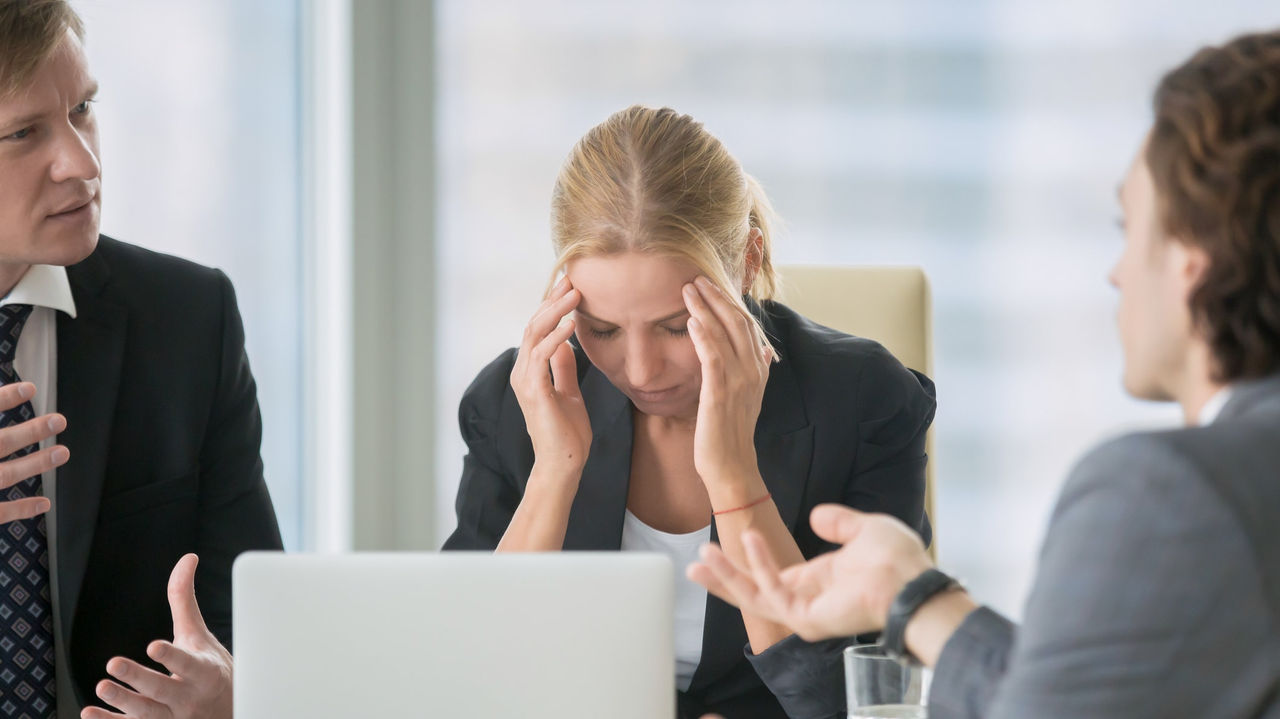 A group of business people sitting at a table with their heads in their hands.