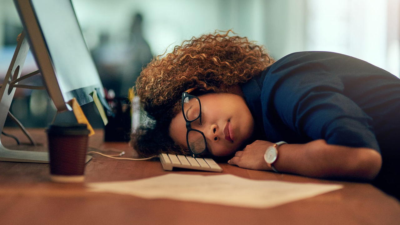 A woman is sleeping on a desk in an office.