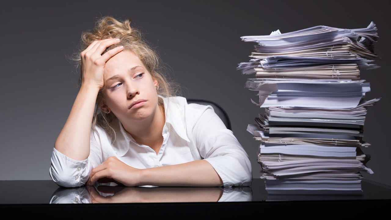 A woman is sitting in front of a pile of papers.