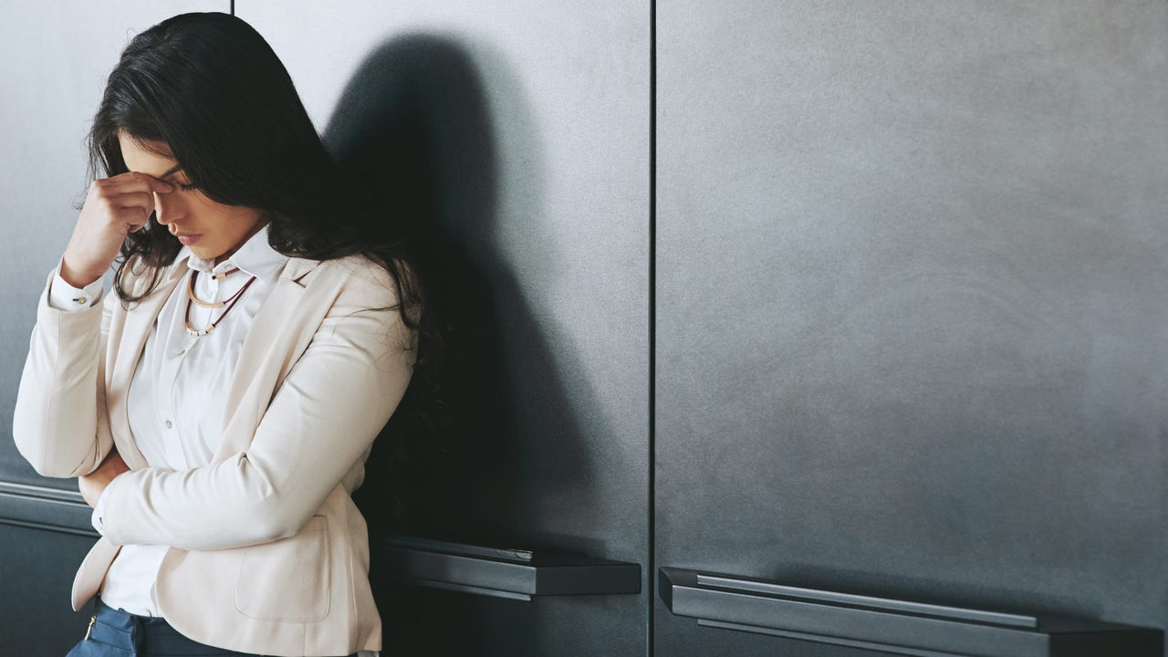 A woman leaning against a wall with her hand on her head.