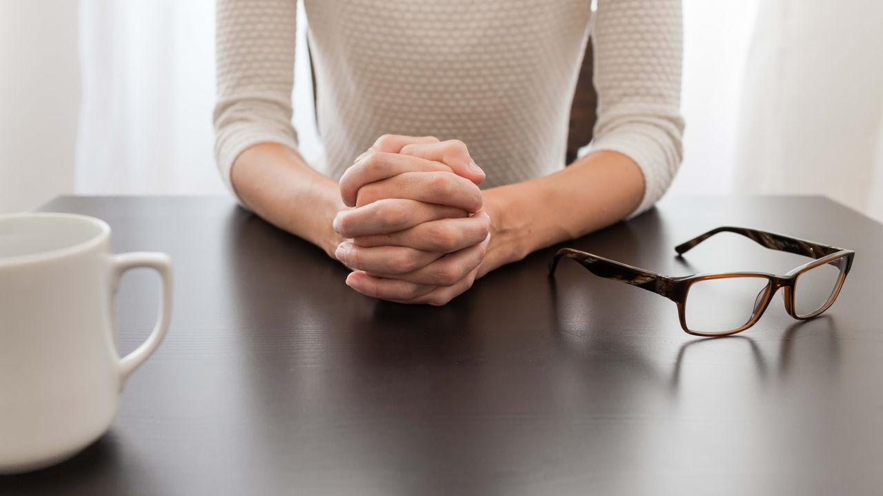 A woman is sitting at a table with glasses and a cup of coffee.