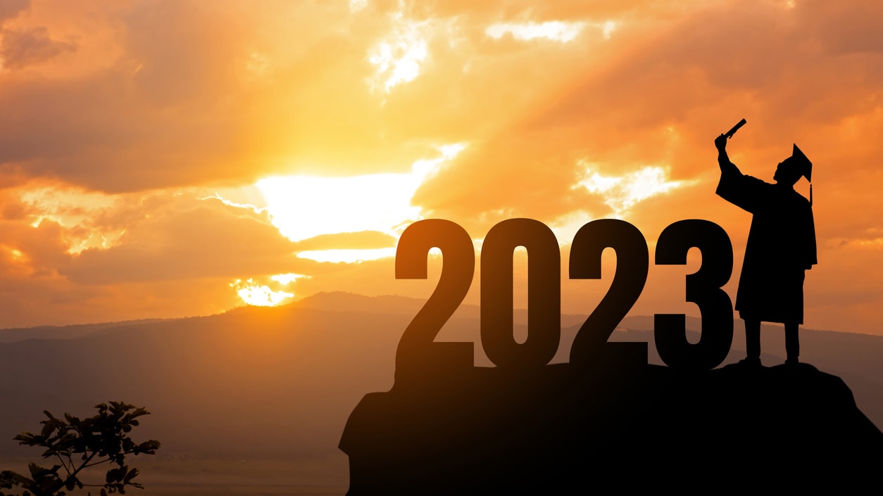 A silhouette of a graduate standing on top of a mountain at sunset.