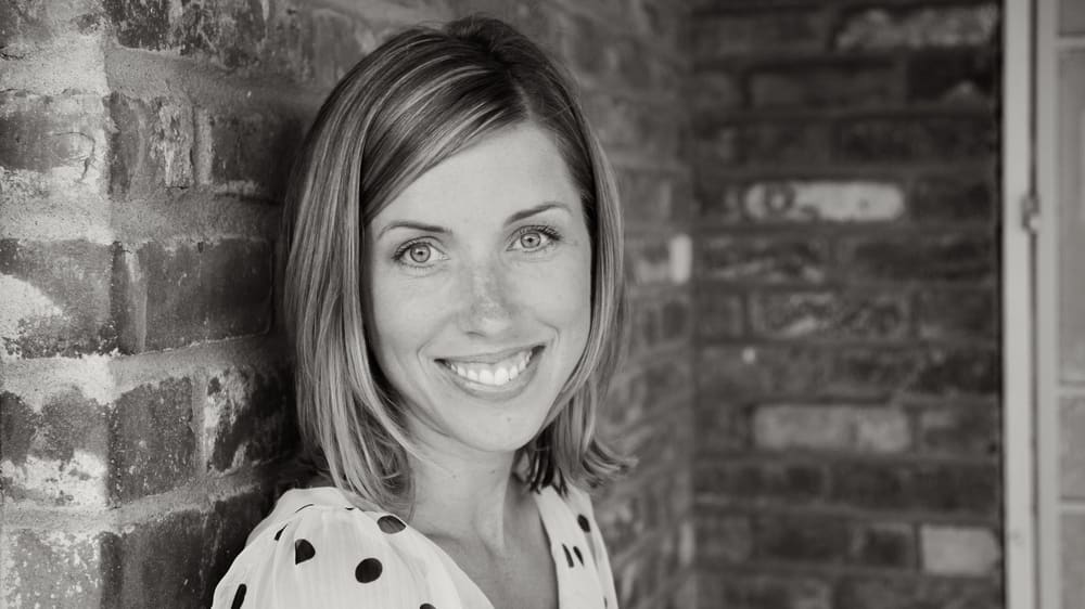 A black and white photo of a woman leaning against a brick wall.
