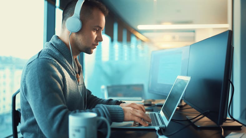 A man wearing headphones is working on a laptop.