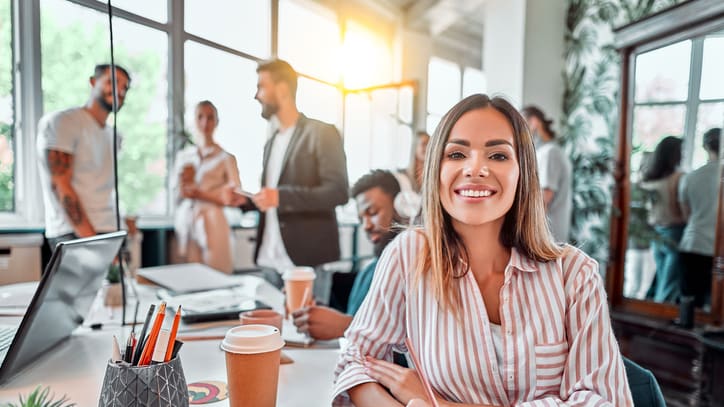 A woman sitting at a desk in an office with a group of people around her.