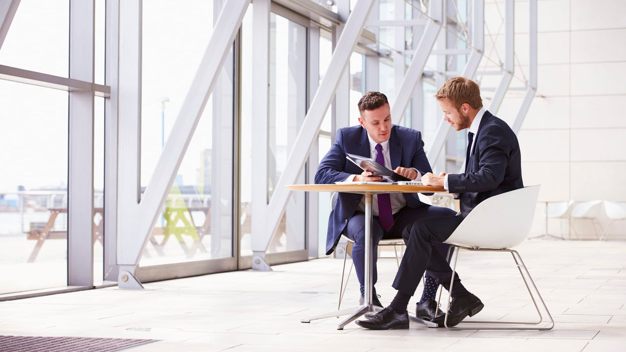 Two businessmen sitting at a table in an office.